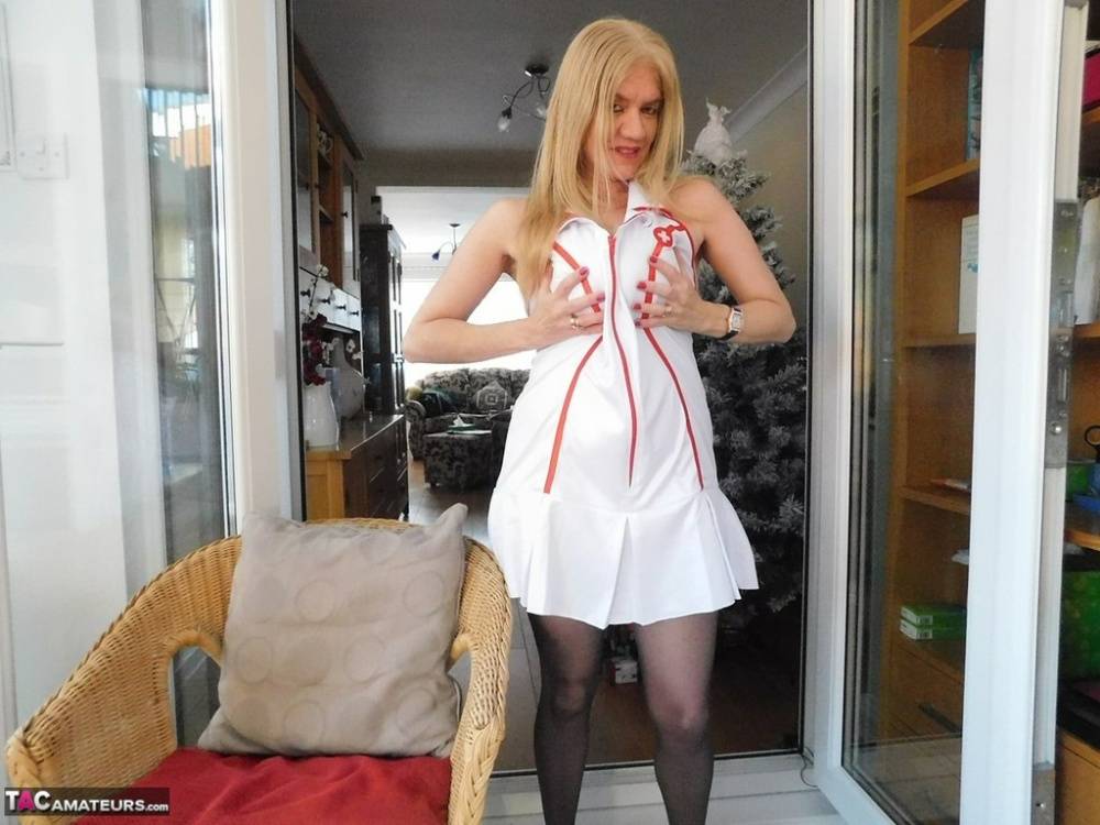 Older British nurse Lily May unzips her uniform on a wicker chair | Photo: 596381