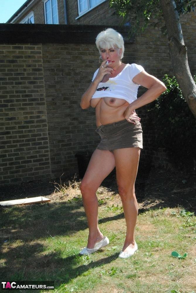 Older platinum blond Dimonty smokes while exposing her tits & twat in a yard - #9