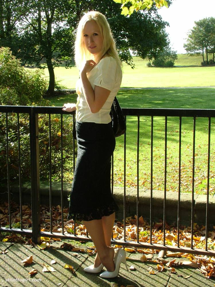 Clothed blonde Iona shows off her white stilettos in a long skirt by a park | Photo: 1218647