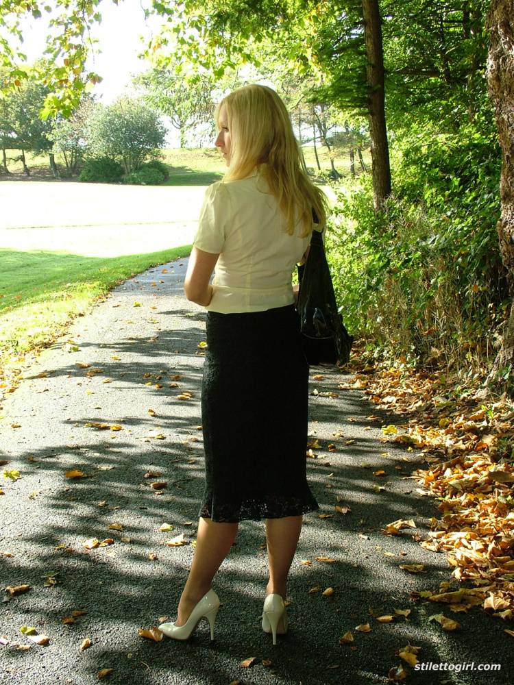 Clothed blonde Iona shows off her white stilettos in a long skirt by a park | Photo: 1218651
